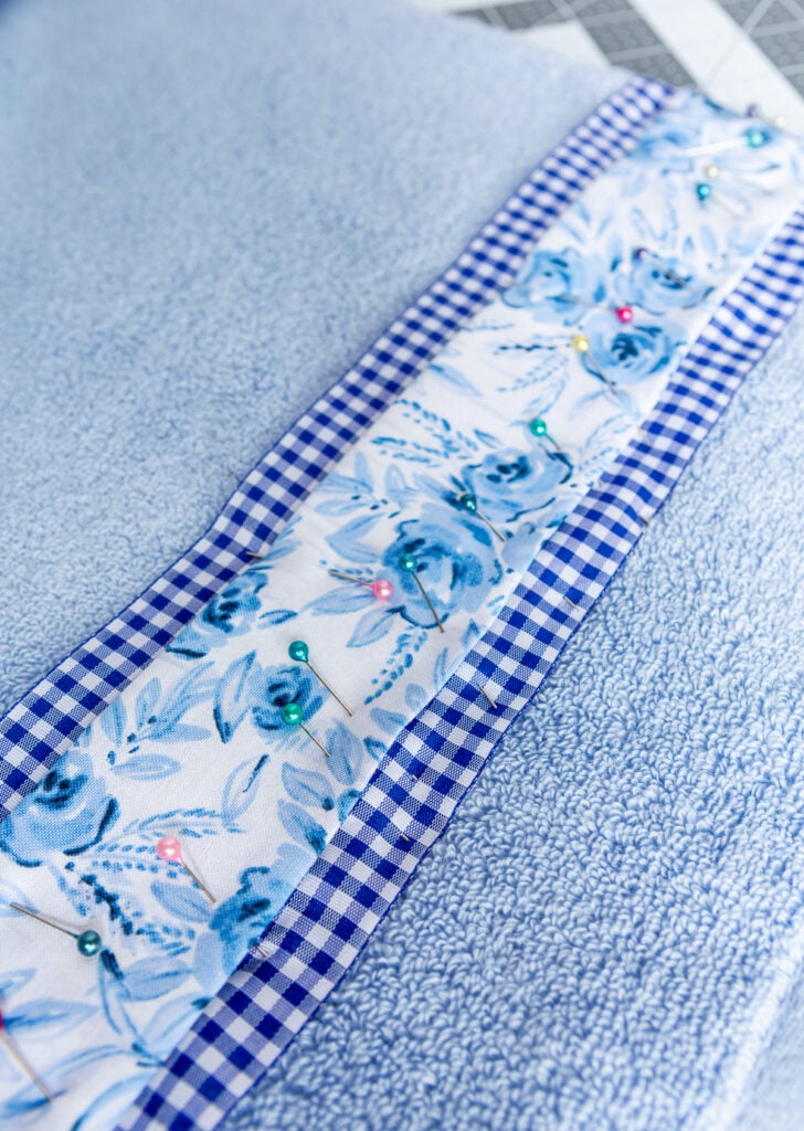 Blue flower fabric and gingham ribbon being pinned onto a bath towel before sewing.
