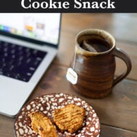 a plate with two cookies on it with a cup of tea and computer on a table.