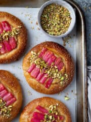 Rhubarb frangipane buns on a baking tray with a bowl of chopped pistachios.