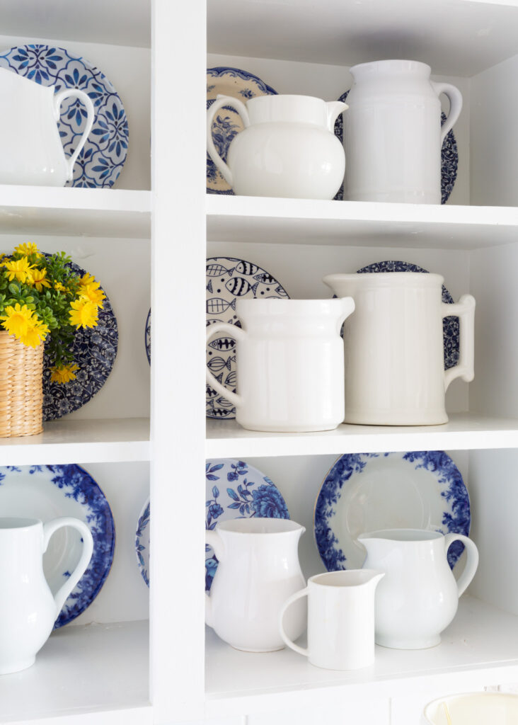 a collection of white ceramic pitchers displayed on open shelves in a kitchen.