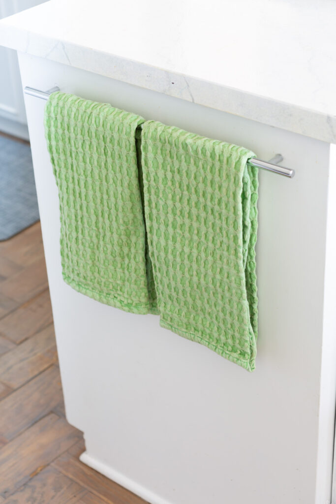 spring green waffle weave dish towels hanging on a towel bar in a kitchen
