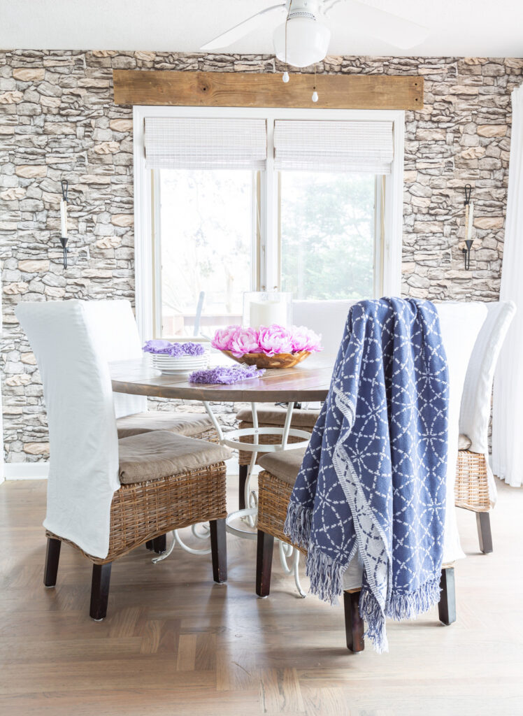 Blue and white throw blanket draped over a white slipcovered kitchen chair around a dining table.