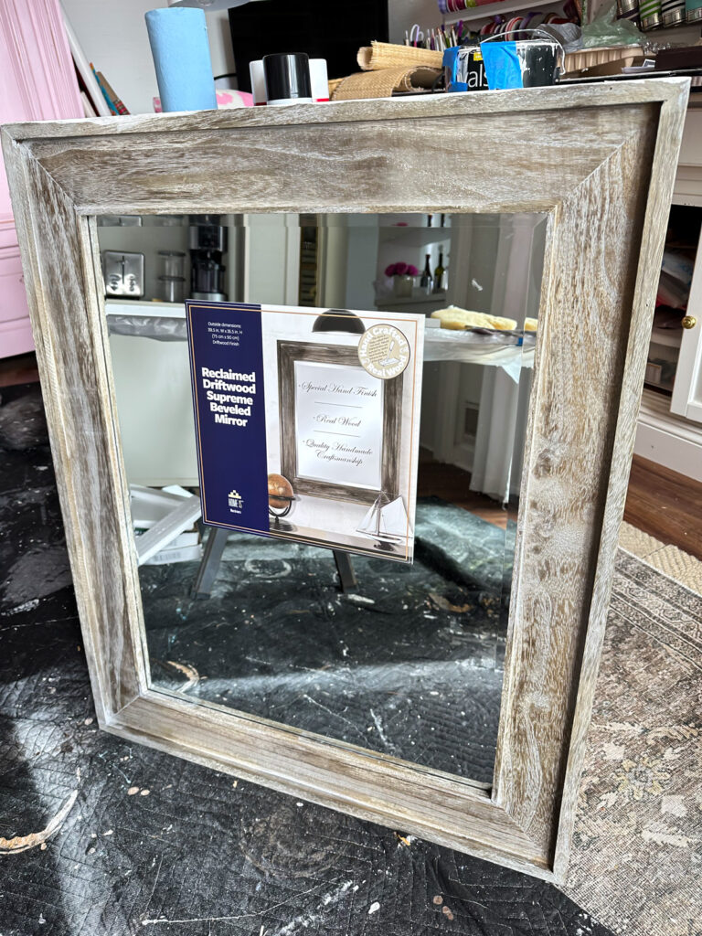 Large wall mirror with a rustic wood frame leaning against saw horses.