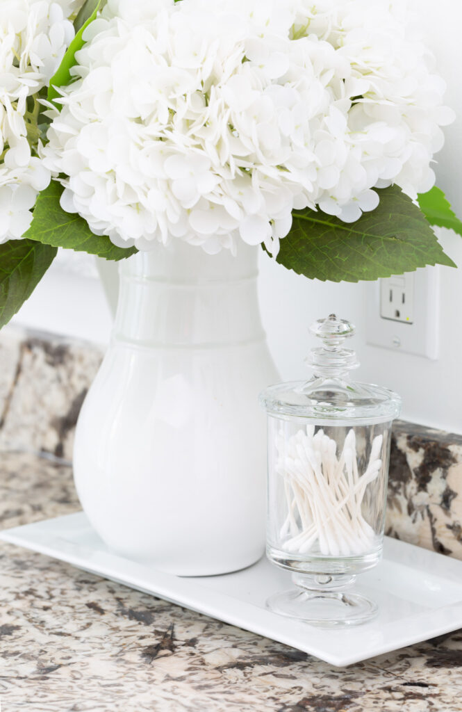 white hydrangeas in a white pitcher on a bathroom counter.