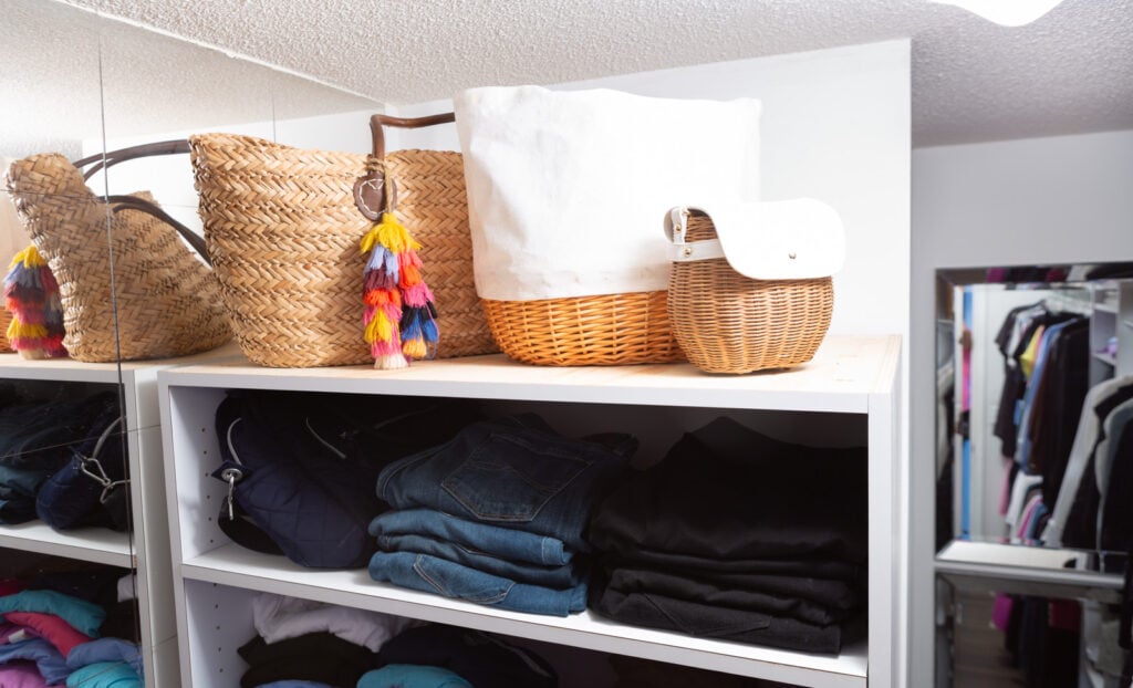 Handbags and totes on top of a built in clothes closet organizer.