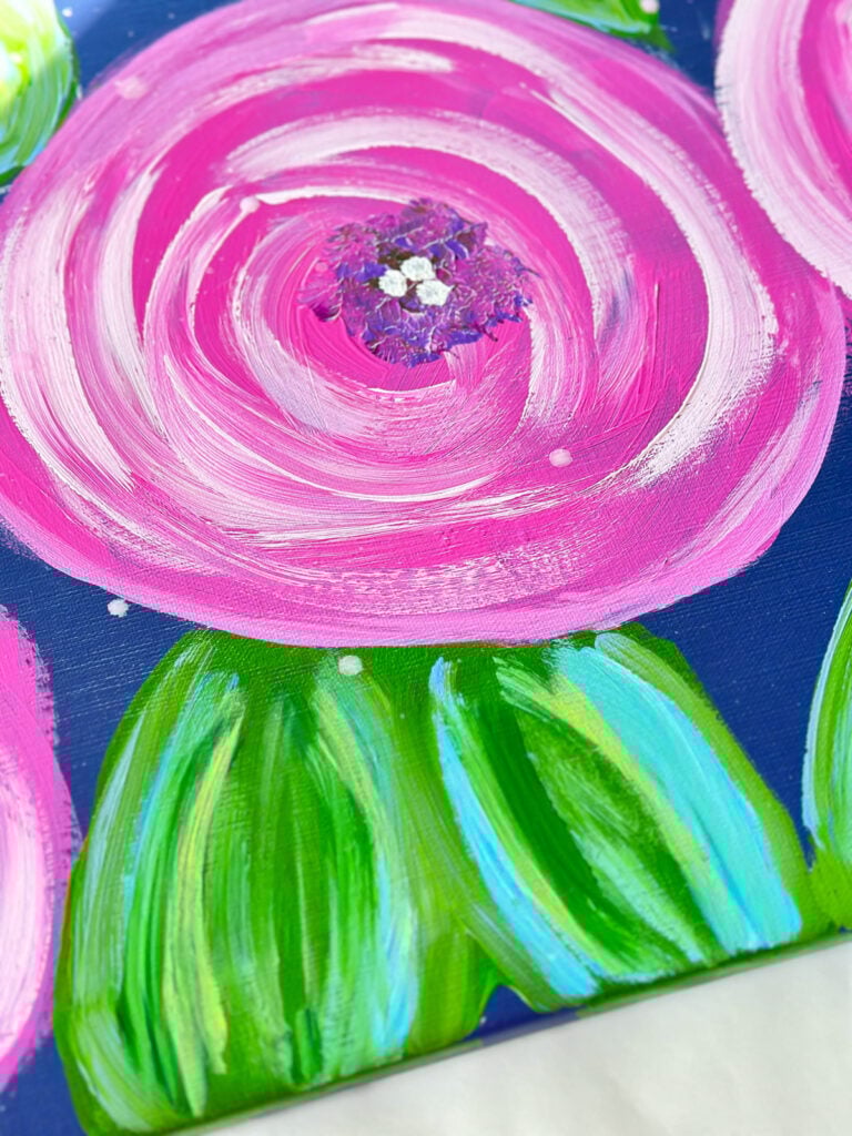 close up of acrylic paint brush strokes used to paint a large pink flower and green leaves on an art canvas.
