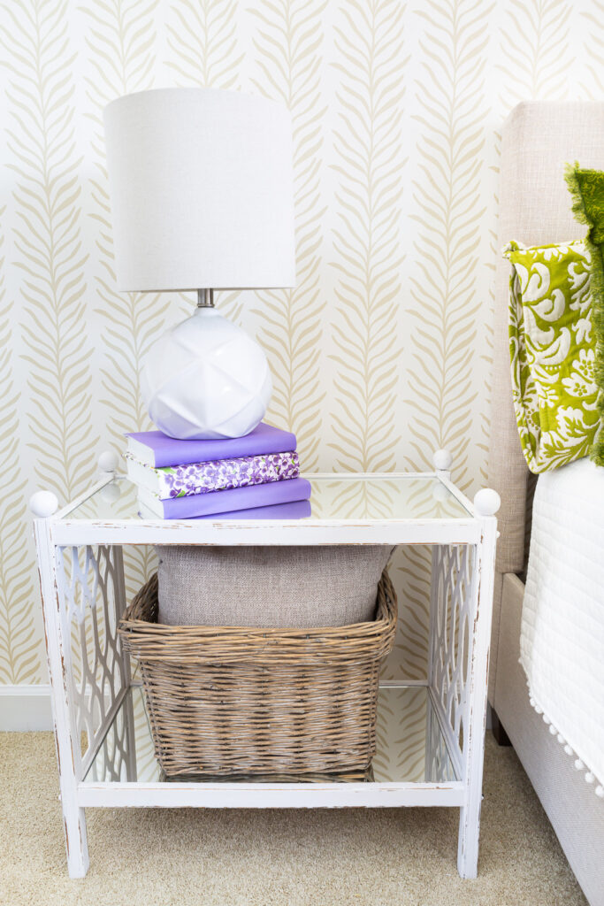 A white night table in a bedroom with an accent wall covered with a Love vs. Design wallpaper pattern called Vine Thread.
