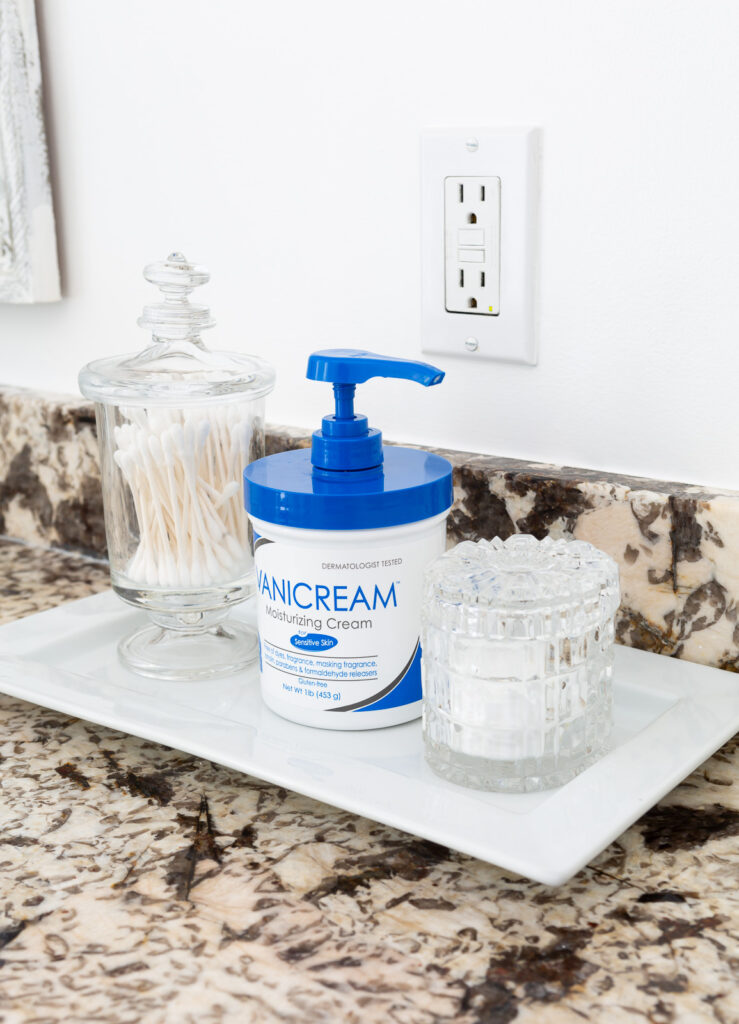 Plastic moisturizing cream container on a white tray in a bathroom.