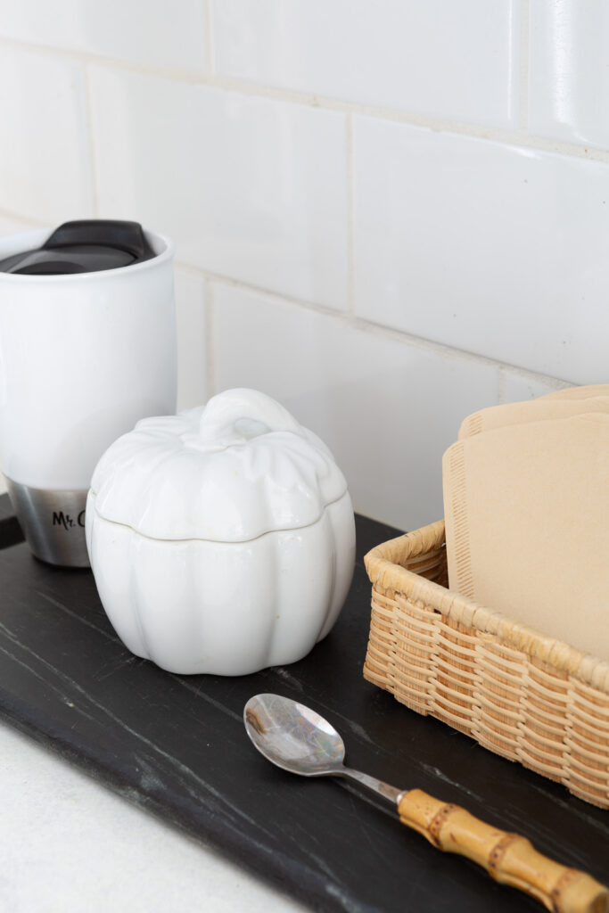 white ceramic pumpkin bowl with lid to hold sugar for the fall season placed on a kitchen counter coffee station.