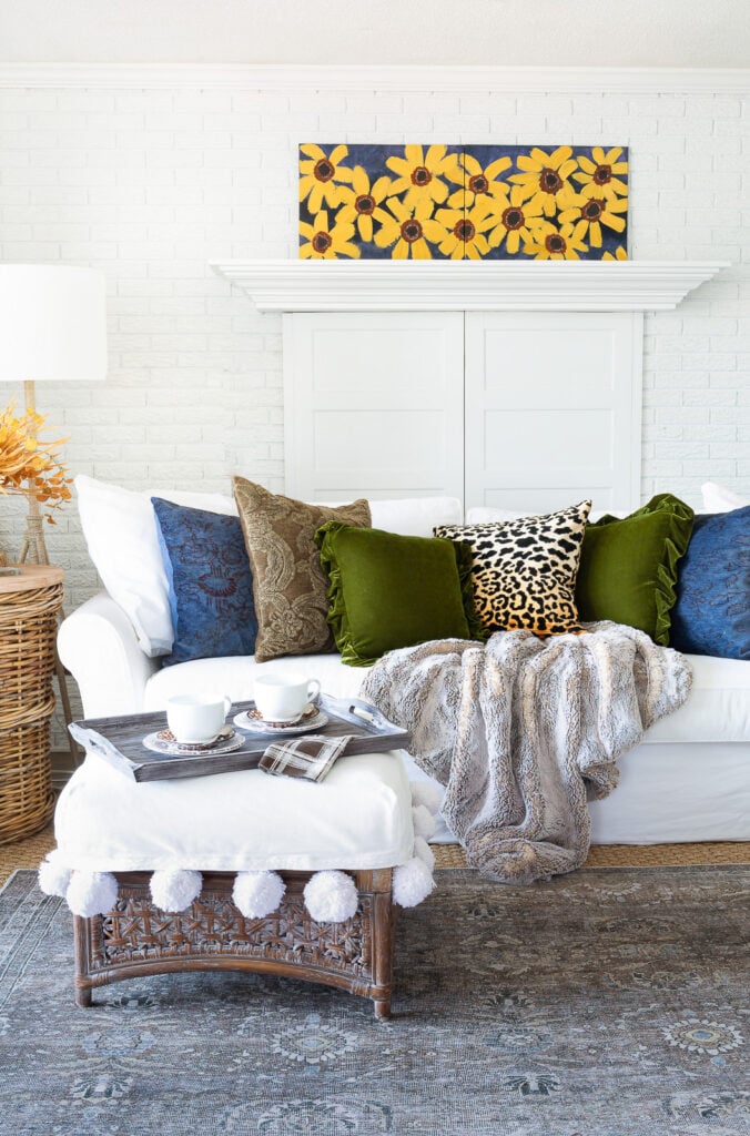 simple fall decor using throw pillows on a sofa in a white room with blue, green and burnt yellow accents.