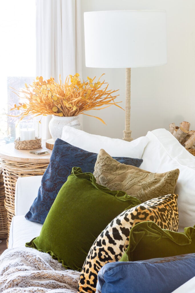 Line up of pretty fall throw pillows on a white sofa with a wicker table and floor lamp at the end.