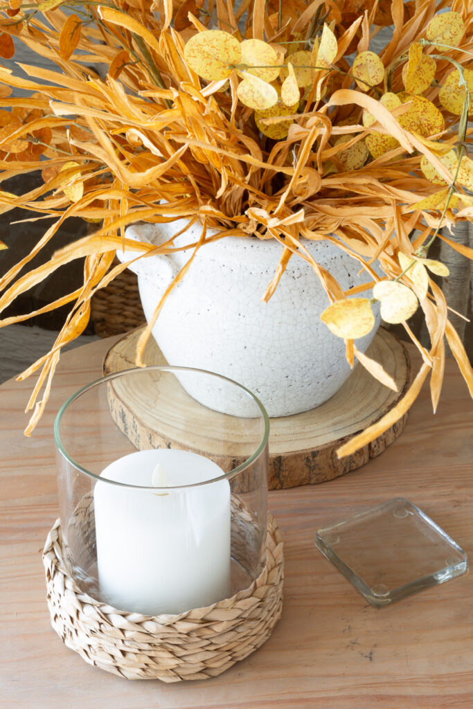 Wood side table with white candle and fall stems in a white crackled surface planter.