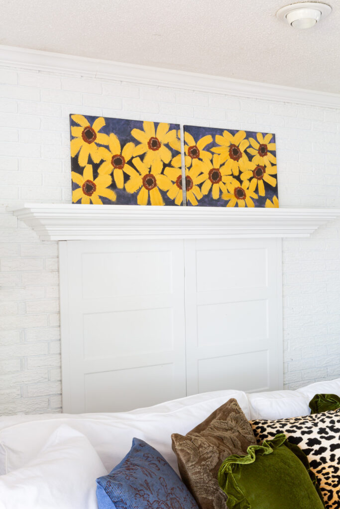 Painted fall flowers on a canvas leaning on a white fireplace mantel.