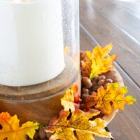 single faux fall leaves around a candle in a wood bowl
