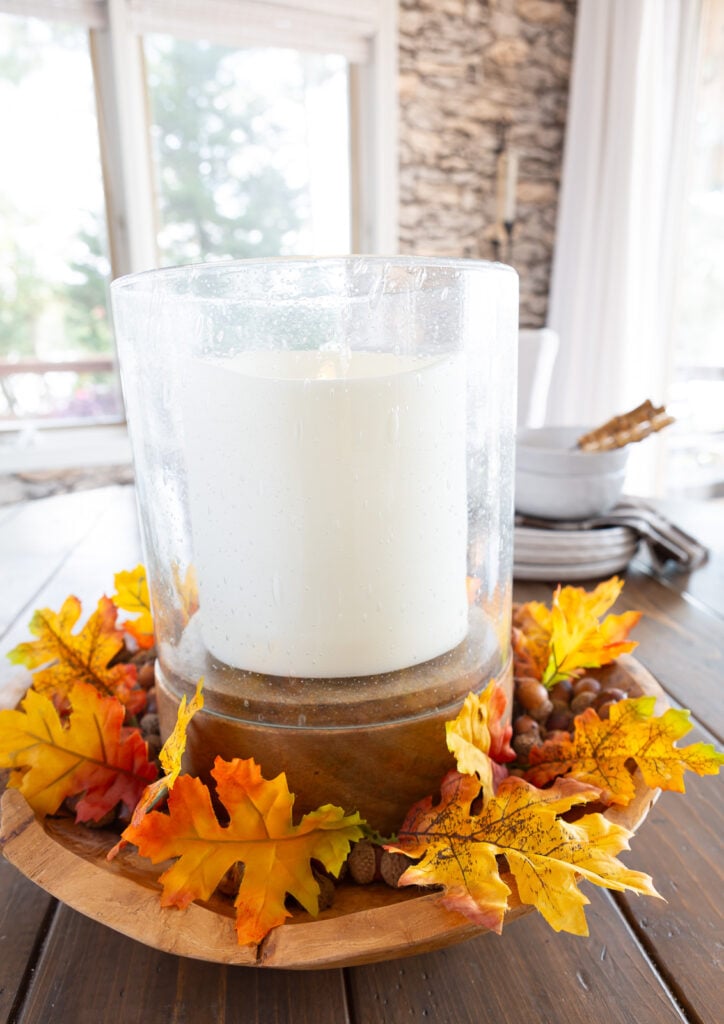 Single faux Maple leaves placed around a large candle in a bowl as a table centerpiece.