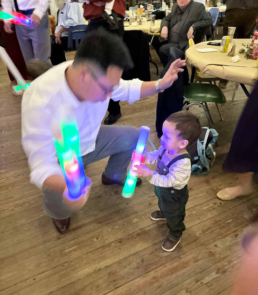 Dad and toddler son dancing with glow sticks at wedding