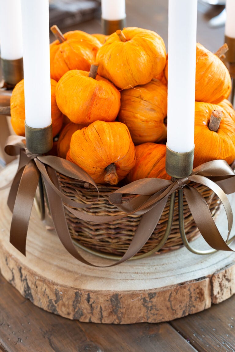 Antique Brass 6 taper candle centerpiece with brown ribbon bows added on wood slice on table. Center has basket filled with tiny paper pumpkins.