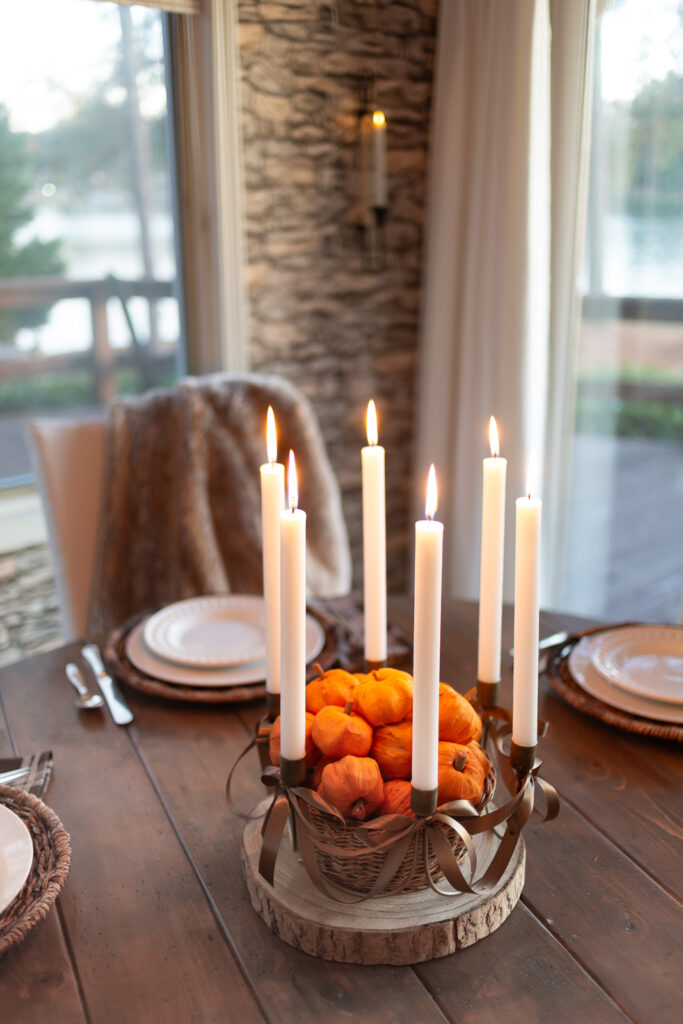 Antique Brass 6 taper candle centerpiece with brown ribbon bows added on wood slice on table. Center has basket filled with tiny paper pumpkins.