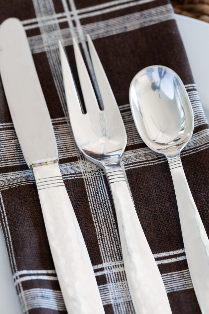 a place setting of Swedish Modern Sterling by Allan Adler on a brown and white table napkin.