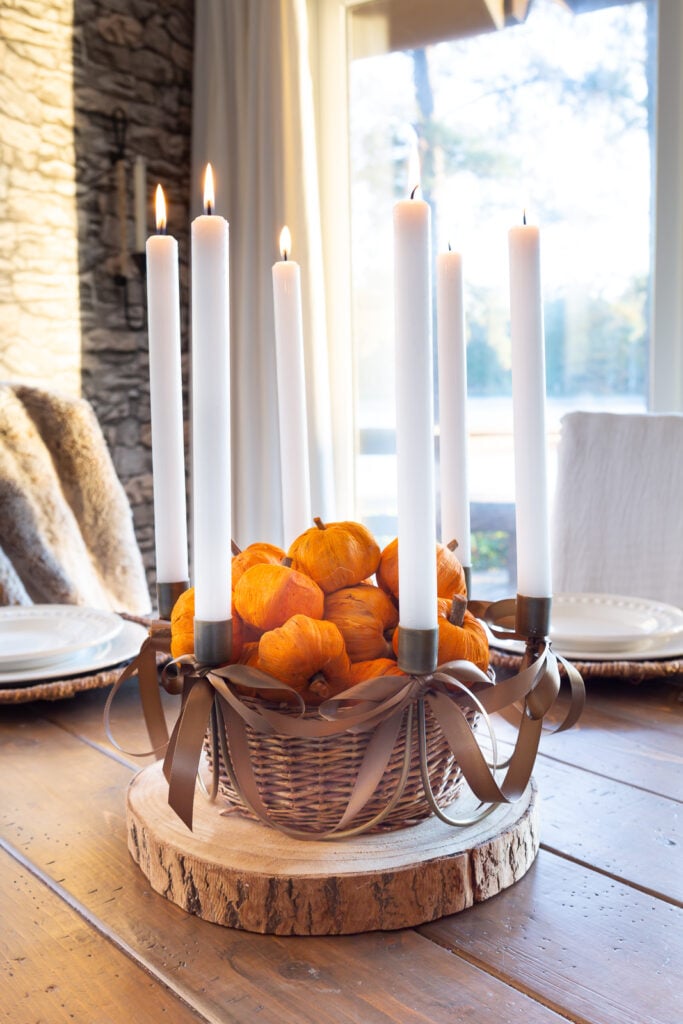 Antique Brass 6 taper candle centerpiece with brown ribbon bows added on wood slice on table. Center has basket filled with tiny paper pumpkins.