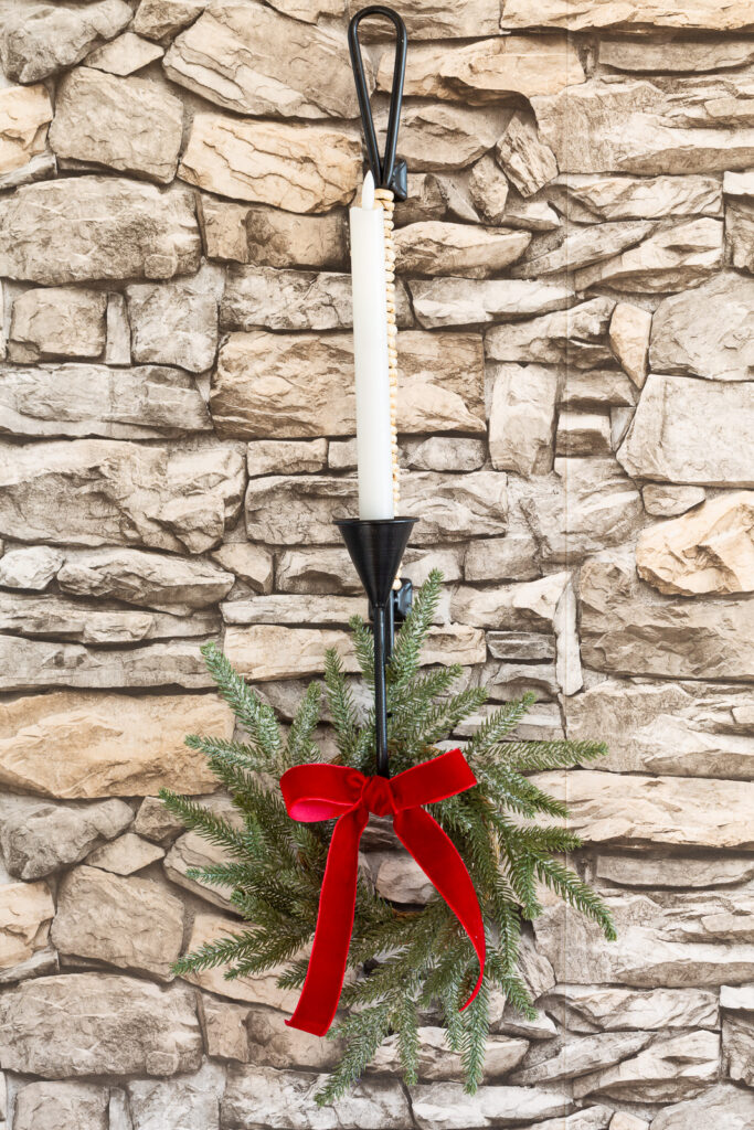 wall candle sconce on stone wall decorated for Christmas with greenery wreath and red velvet ribbon.
