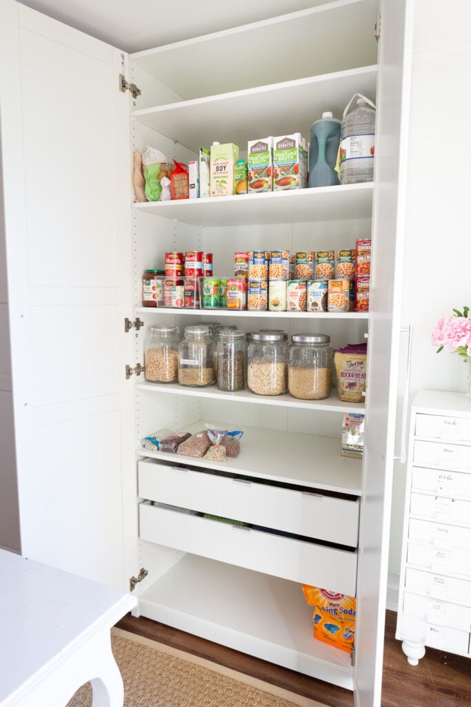 IKEA PAX storage closet in white fitted with shelves and 2 drawers to hold food and pantry staples in a multi-purpose room in a home.