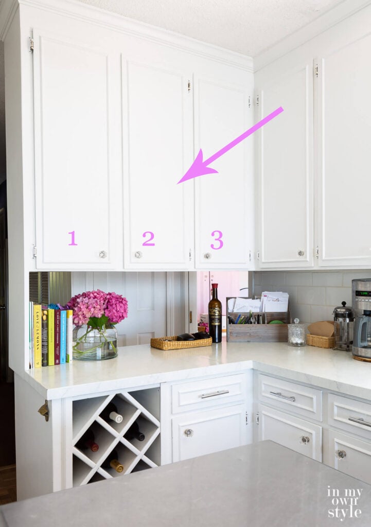 arrow pointing to 3 upper wall cabinets in a small kitchen that are going to be removed.
