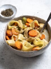 A bowl of vegan chicken noodle soup with a bowl of dried thyme.