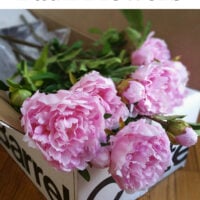Pink peonies in a crate and barrel box. Text overlay says How to make faux flowers look. real.