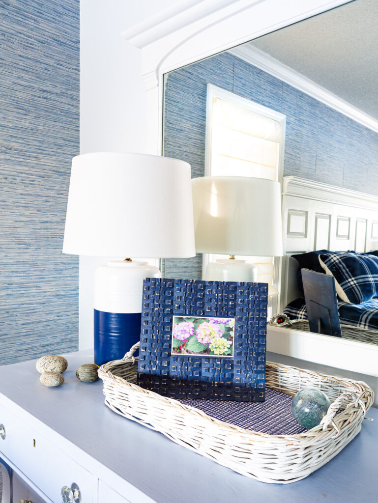 Blue and white lamp and blue picture frame on a blue dresser in a bedroom.