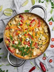 A pan of Thai style coconut tofu surrounded by herbs, lime slices and chillies.