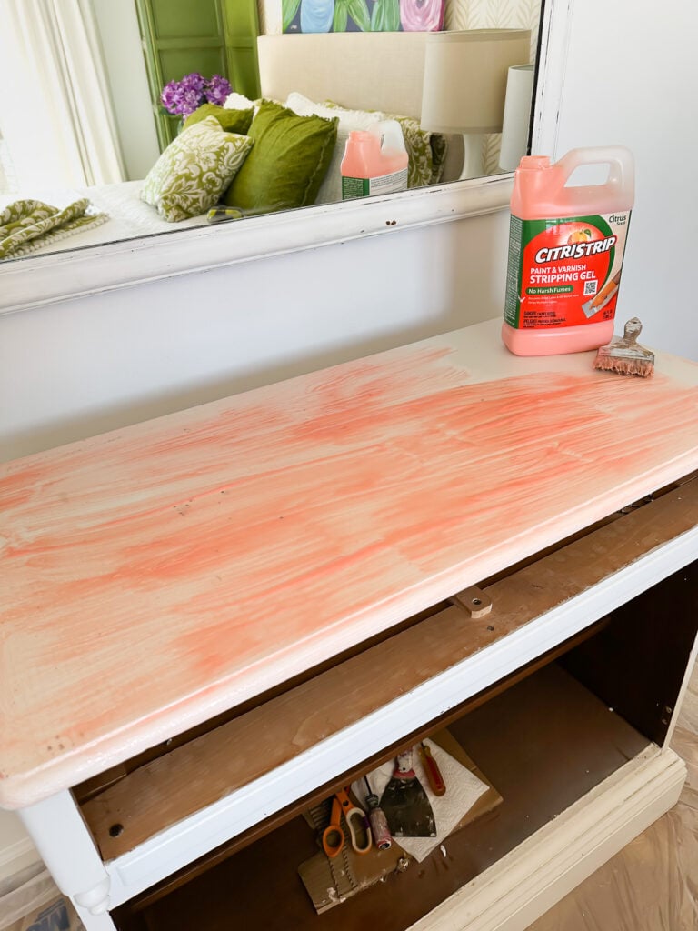 a bottle of citrastrip and a brush on top of a sideboard that has Citrastrip on it to start the paint removing process.