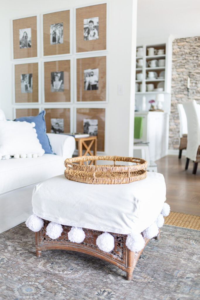 Round rattan tray on white slipcovered ottoman in a living room.