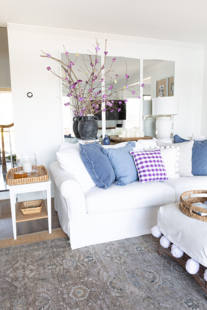 White sofa on mirror wall in living room with blue and purple toss pillows on it.