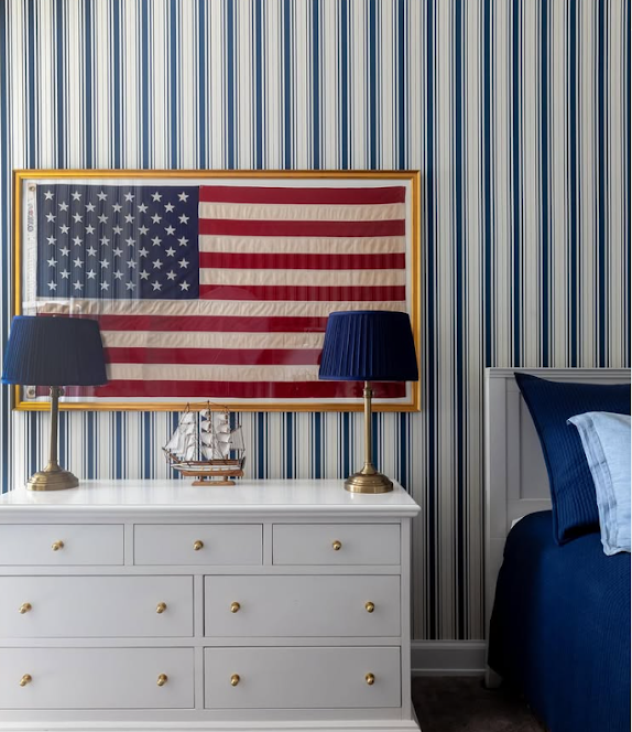 Framed American flag hanging on a blue and white striped wall in a bedroom.