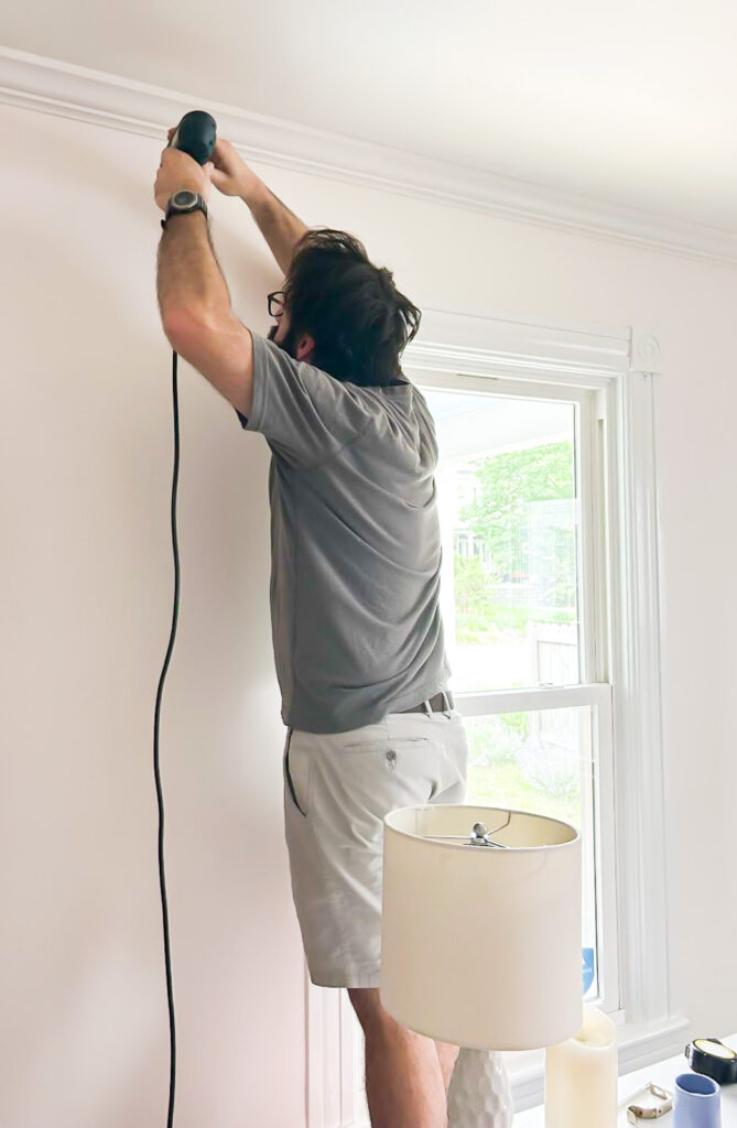 man drilling holes in wall to hang a curtain/drapery rod.