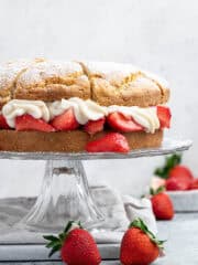 Vegan strawberry shortcake on a glass cake stand on a marble board.