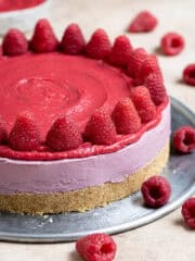 Vegan raspberry cheesecake topped with fresh raspberries on a metal plate.