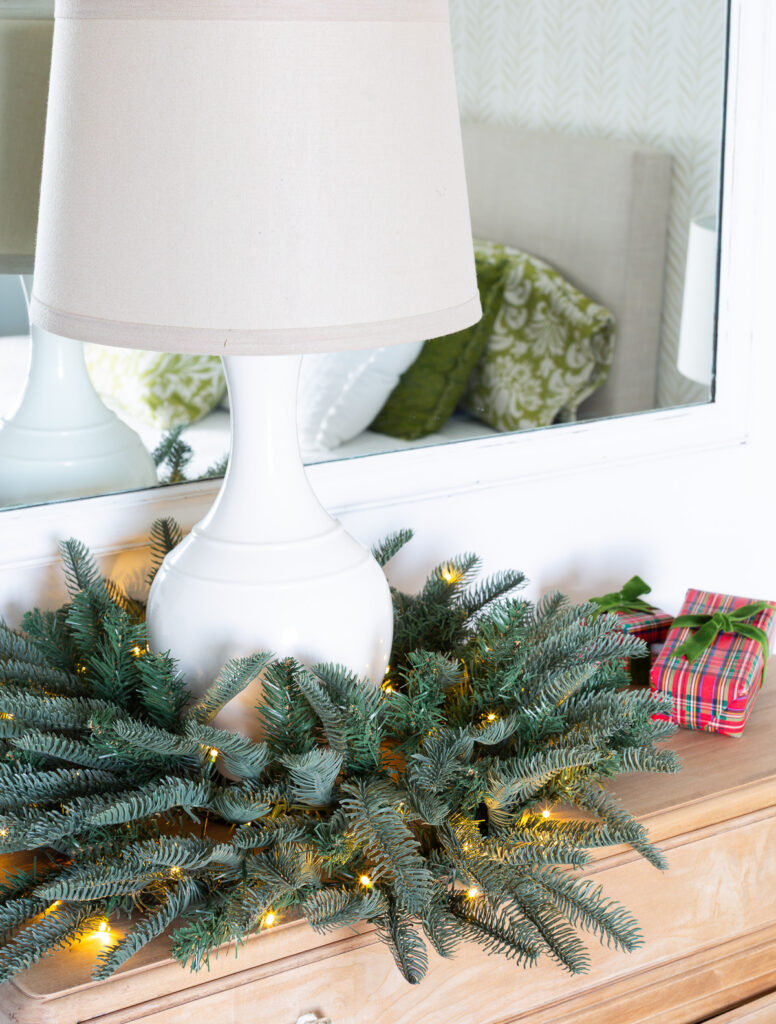 Table lamp on sideboard with a lit Christmas wreath around the base.