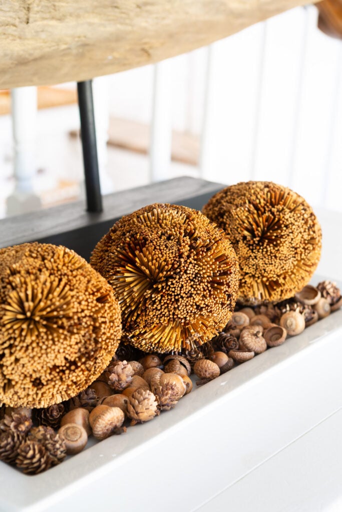 3 brown textured spheres on a bed of acorns on a white ceramic tray on a sideboard.