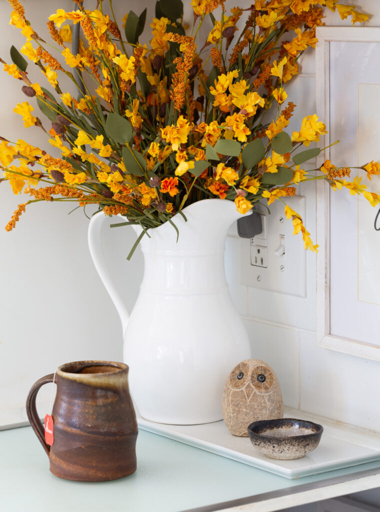 white ceramic pitcher on kitchen counter filled with fall foliage.