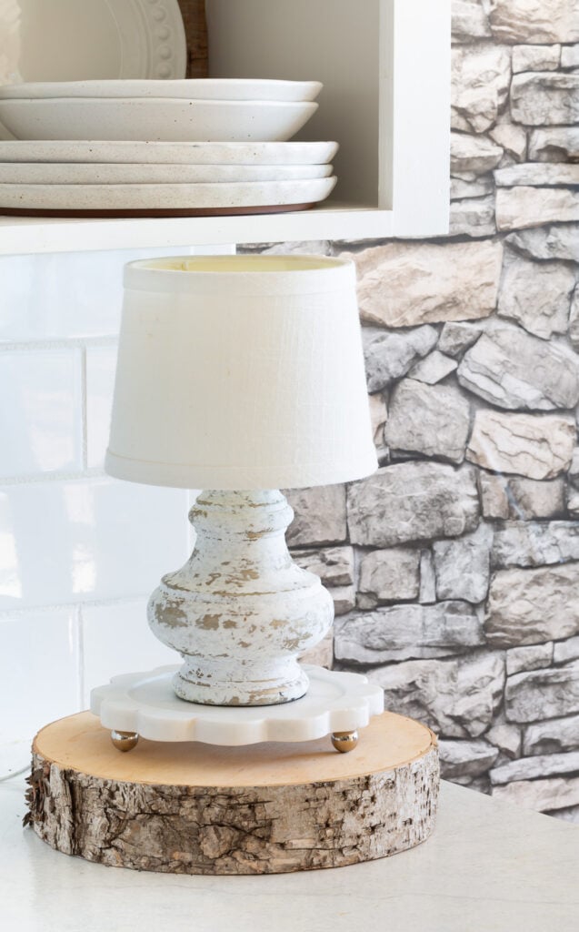 aged white lamp on a marble trivet on top of a wood tree slice for fall decor on a kitchen counter.