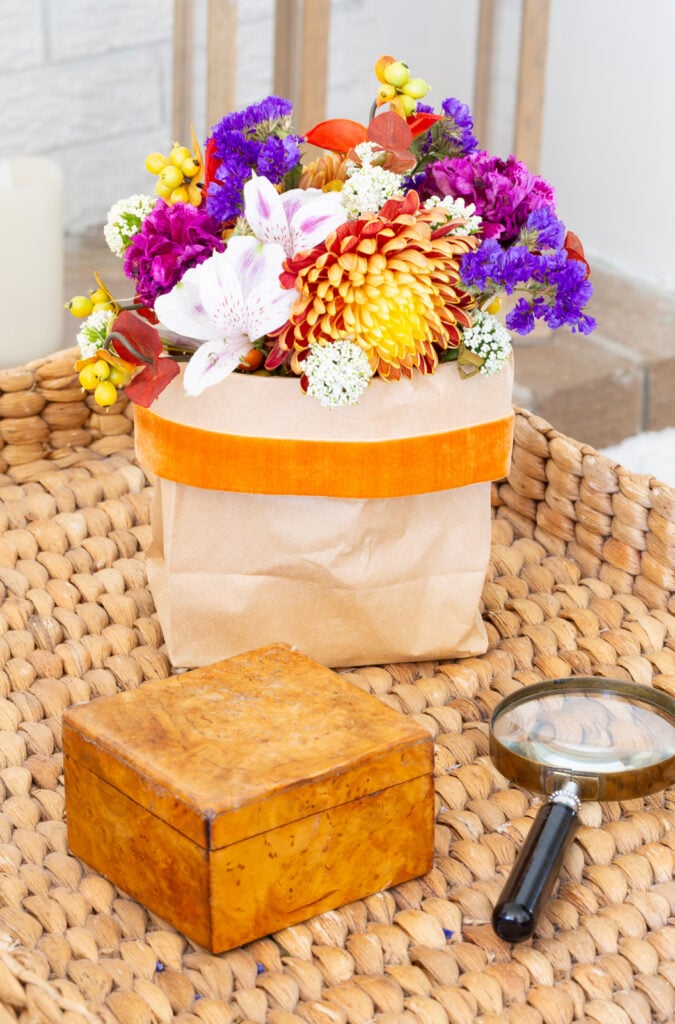 fall flowers vase placed in a brown paper bag with orange velvet ribbon on a side table.