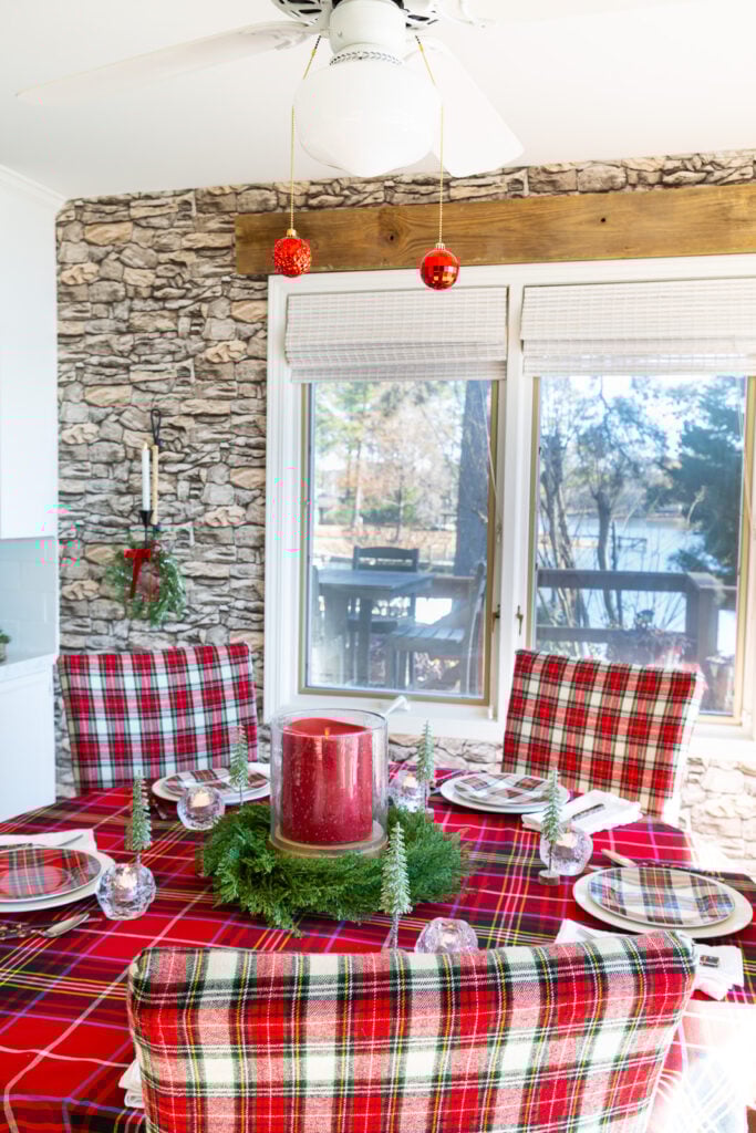 Red plaid decorated kitchen for Christmas with 2 red ornaments hanging at the end of the pull chains on the light fixture above the dining table.