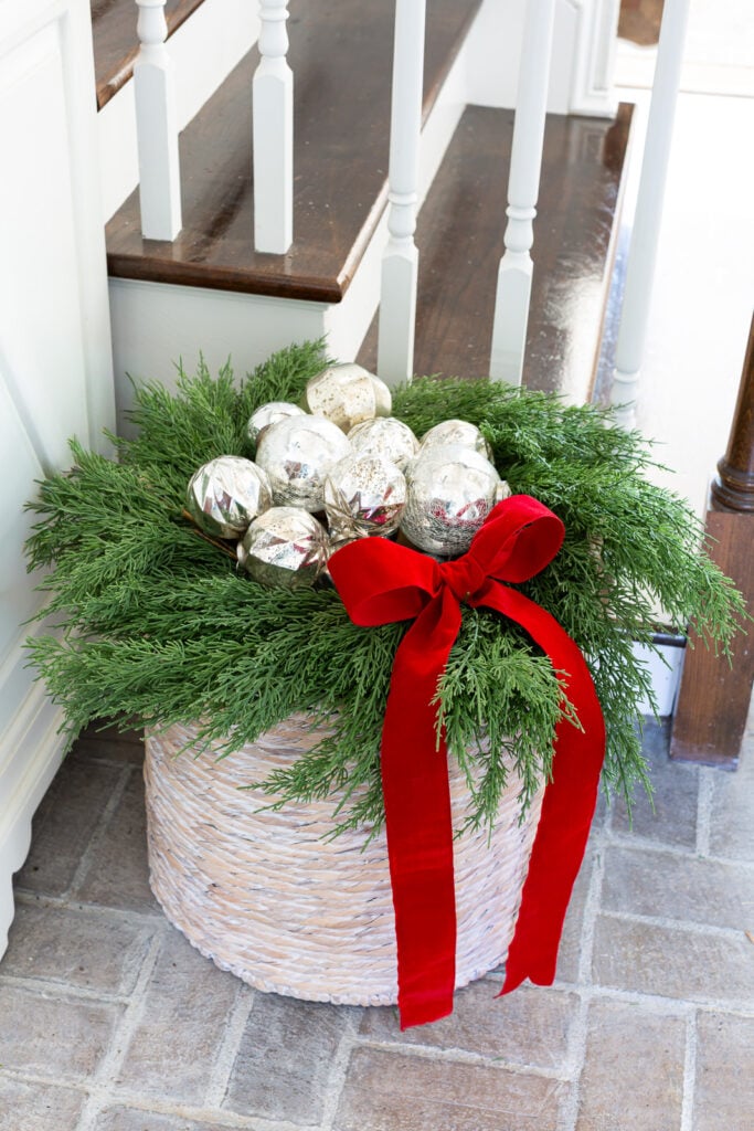 A collection of silver ornaments nestled in a wreath on top of a large woven floor basket.