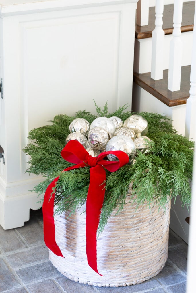 Silver Christmas ornaments nested in a wreath on top of a large woven floor basket.