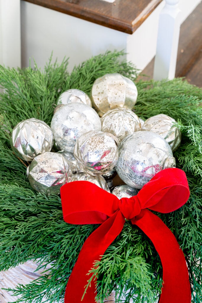 close up of a collection of silver ornaments nestled in a wreath on top of a large woven floor basket.
