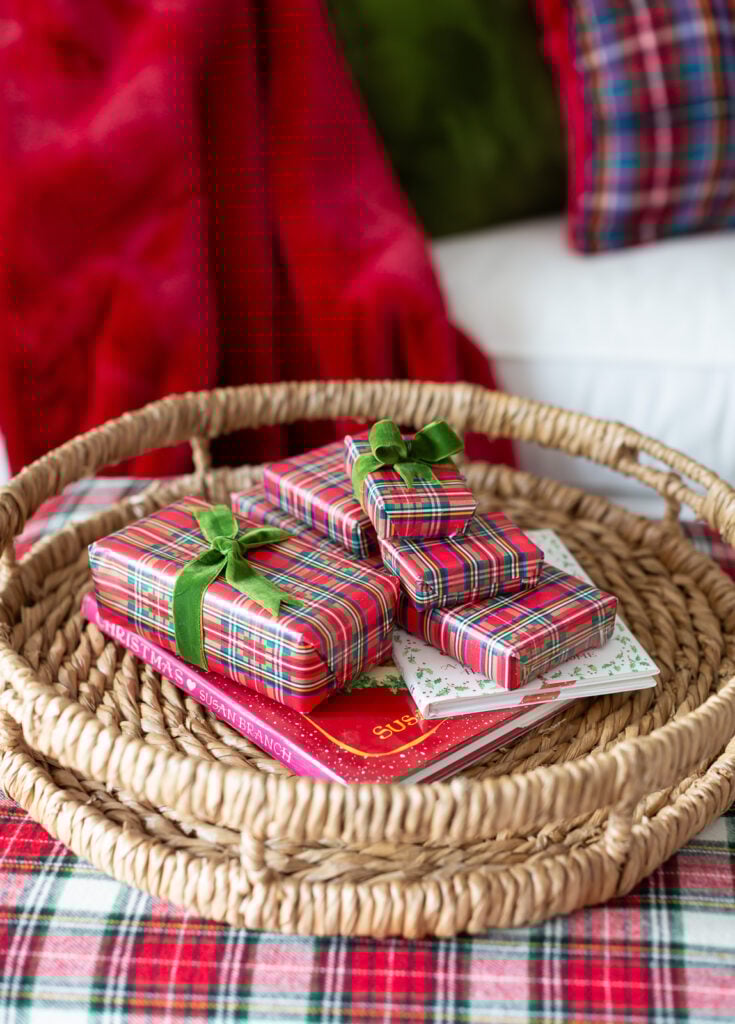 a stack of small plaid gift wrapped boxes on a woven round tray on a plaid covered ottoman.