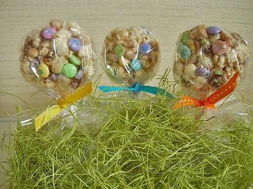 Popcorn-Cake recipe made into lollipop shapes with sticks poked into them. Ribbon tied around sticks and placed on Easter grass.